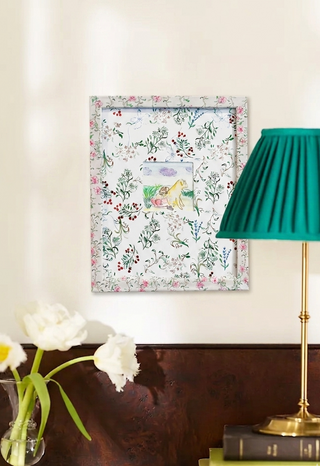 Floral art print on a wall with a green lamp and white flowers in the foreground.