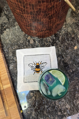 Cocktail with a lime wedge on a bar with a bee-themed napkin.