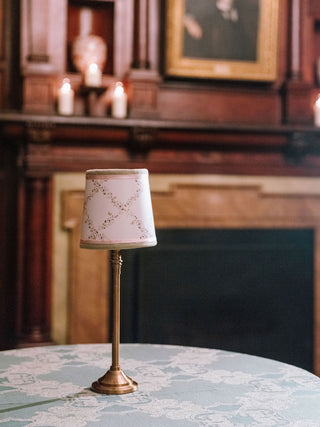 Small lamp with a decorative shade on a table in a room with candles and a painting.