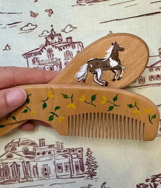 Wooden comb with horse design held over a patterned fabric background