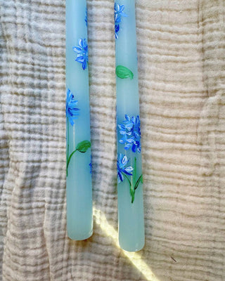 Two light blue candles with floral designs on a textured fabric background