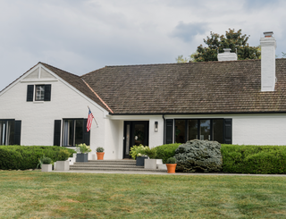 White house with black shutters and a flag on a cloudy day