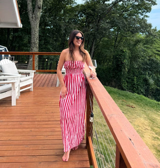 Woman in a red and white striped dress standing on a wooden deck with greenery in the background