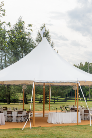 White tent set up for an outdoor event with tables and chairs under a cloudy sky.
